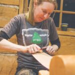 A woman uses a spokeshave to make a paddle at the Canadian Canoe Museum
