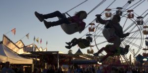 People on the mechanical swing ride at a fairground, with ferris wheel in the background