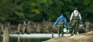 Two anglers carrying tackleboxes walk along the shore