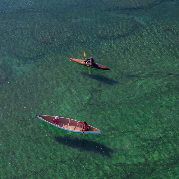 Drone view of a kayak and canoe paddling through clear, shallow water