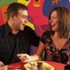 A man and a woman share a meal with a cubist-style mural in the background