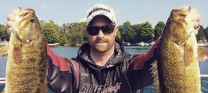 A man in a ballcap holds up two freshly caught fish