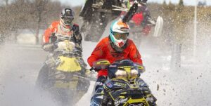 Four snowmobiles kick up a fine haze of snow