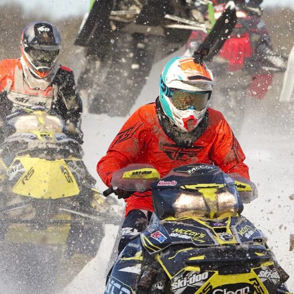 Snowmobilers race towards the camera in a flurry of snow