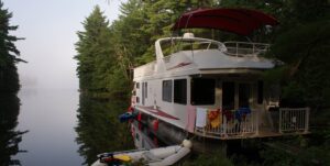 A houseboat moored at a dock with a raft tied up beside it
