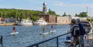 Three people on paddleboards pass through a river in the middle of a town