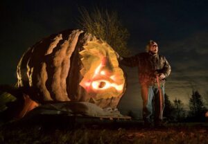 A man stands with his hand on a gigantic carved jack o' lantern