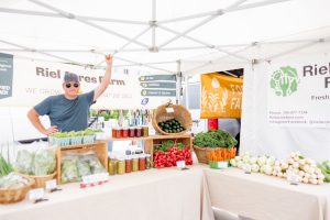 A man works at a farm stand lined with fresh vegetables and preserves
