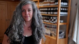 A woman stands in front of a shelf of small bottles