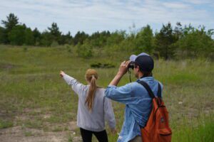 A person with binoculars looks towards where another person is pointing