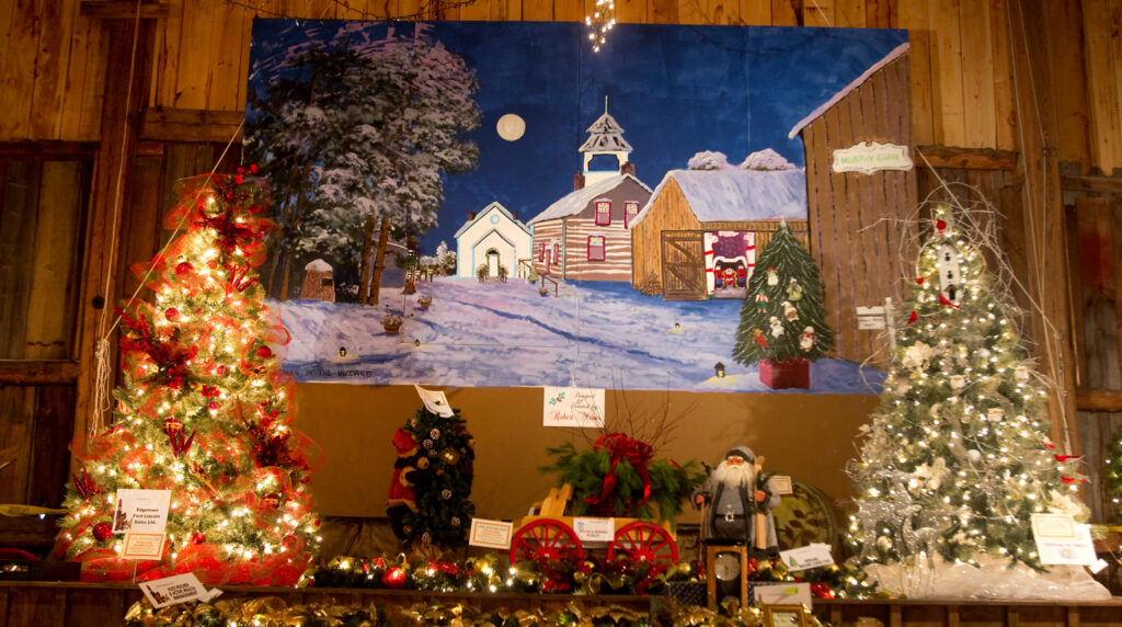Closeup of a Christmas display, featuring a painting of a winter scene bracketed by Christmas trees on either side