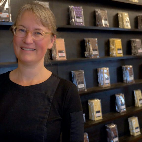 Angela Roest of Centre & Main Chocolate Co. stands in front of a wall of her chocolate bars
