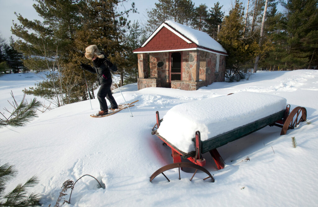 A person sets out on snowshoes from a small cabin