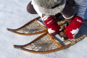 A person bends to fix their traditional snowshoe
