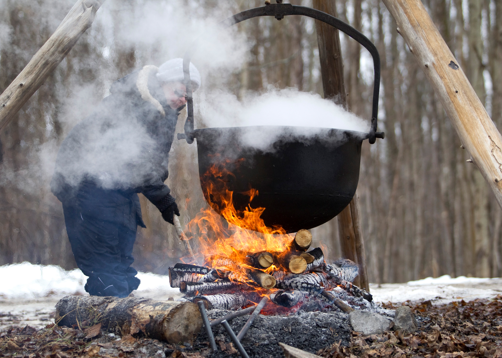 A person boils maple syrup over a fire