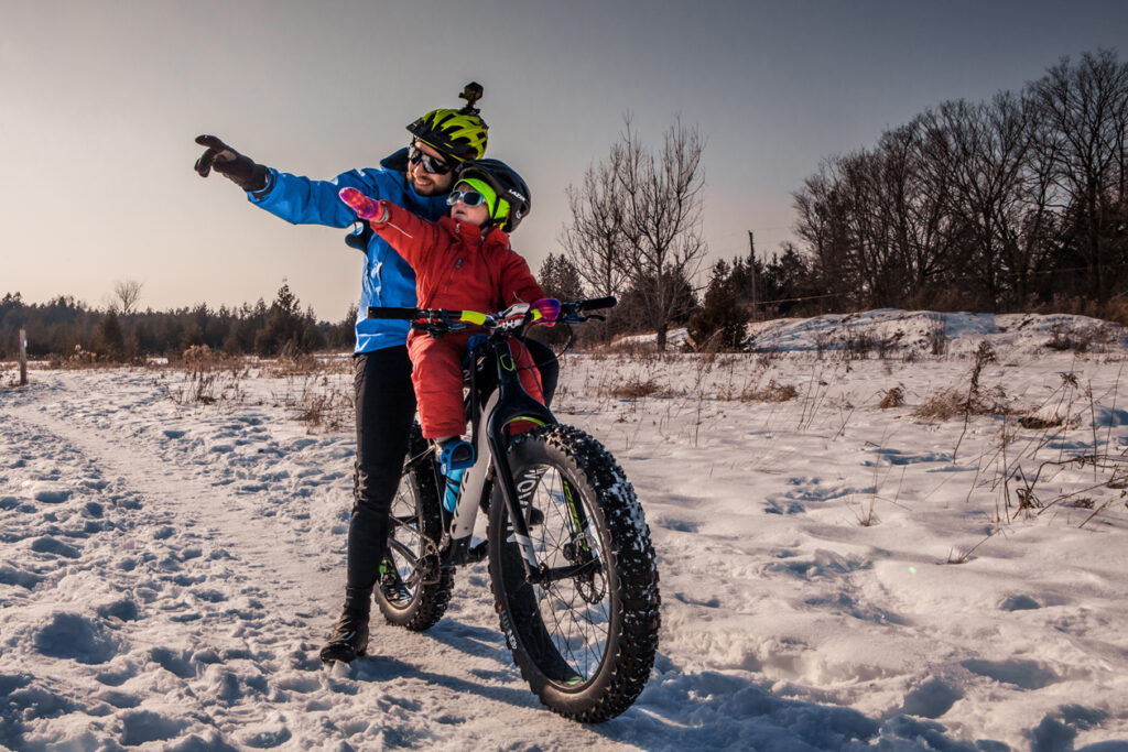 A man rides a fat bike in winter with a child in the seat in front of him