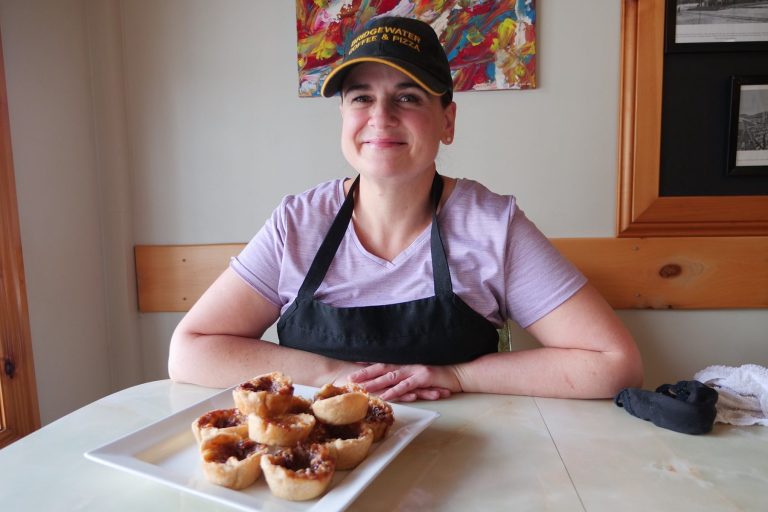 A smiling woman sits with a plate of butter tarts