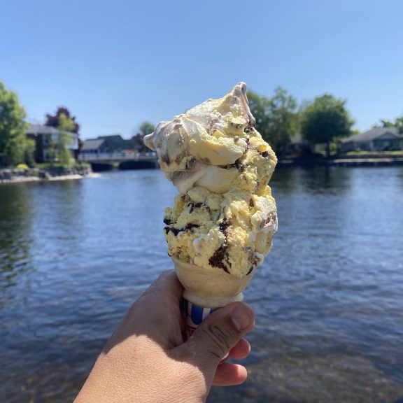 A hand holds ice cream in front of a lake view