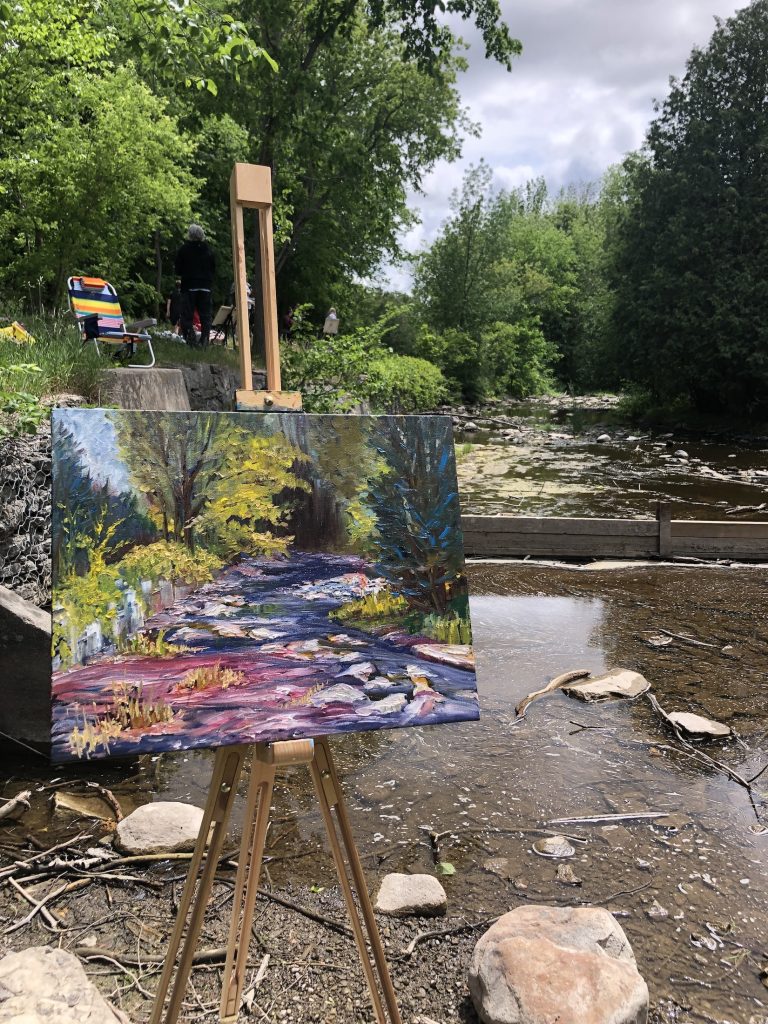 A landscape painting sits in the setting that inspired it, a low creek bed