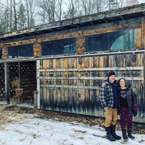 A couple stand beside a sugar shack in late winter