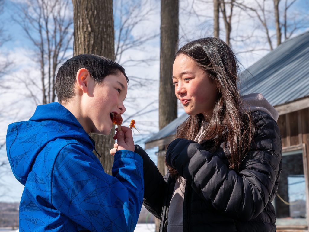 A young boy and a girl smile while eating maple taffy