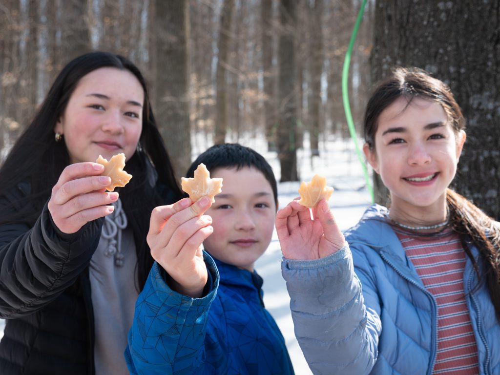 Three young people hold out leaf-shaped maple candies to the camera