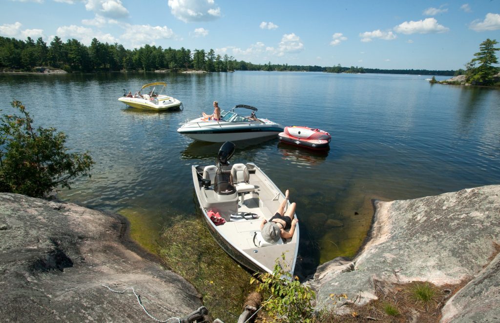 Three motorboats float near a rocky shore, people lounging in them