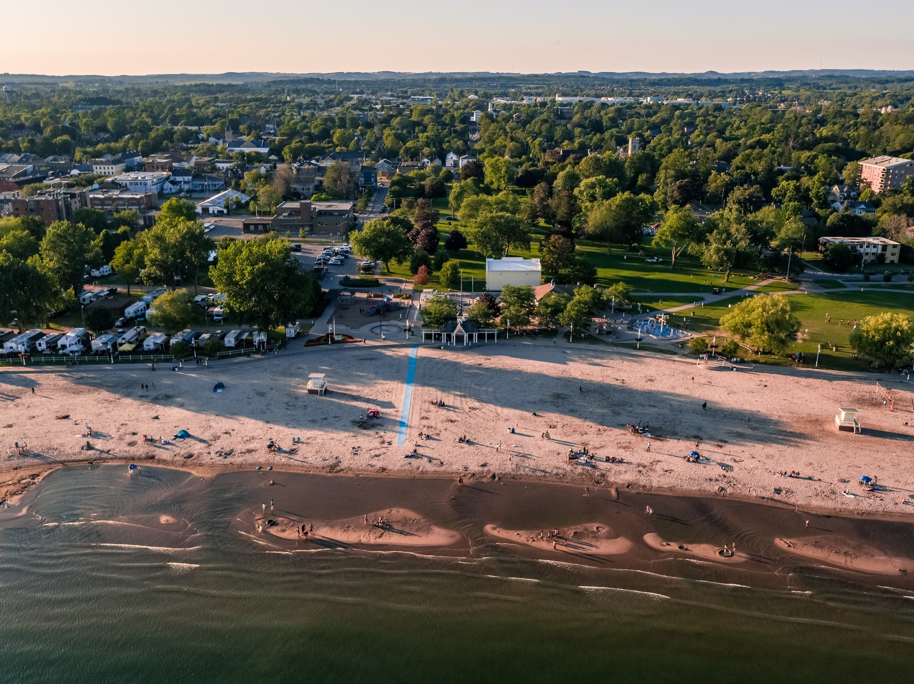 Aerial view of busy, sandy beach in summertime, with blue accessibility mat visible in centre