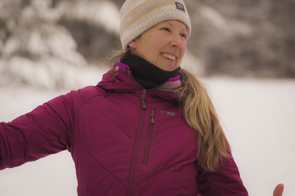A smiling person in a purple jacket and white toque against a snowy background