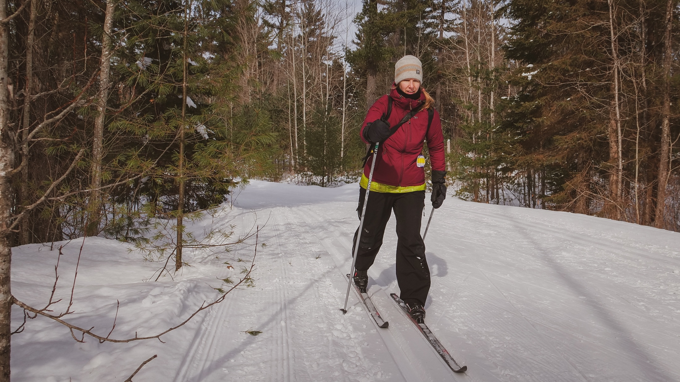 A person in a purple jacket and toque cross-country skis along a snowy trail