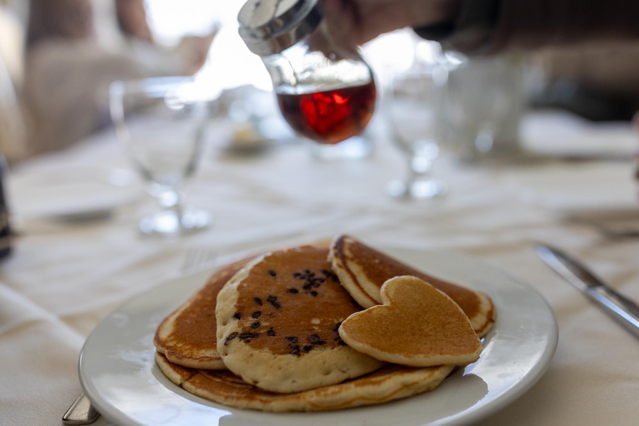 Stack of pancakes, with hand about to pour carafe of maple syrup over it