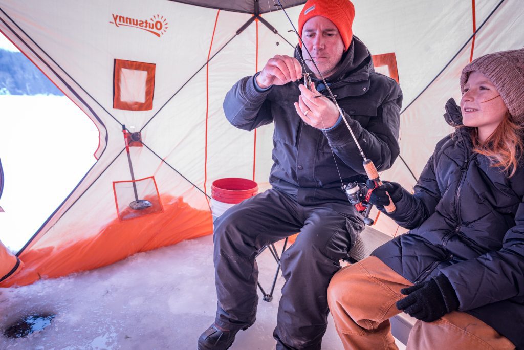 A man in an ice hut baits a hook while a young girl looks on