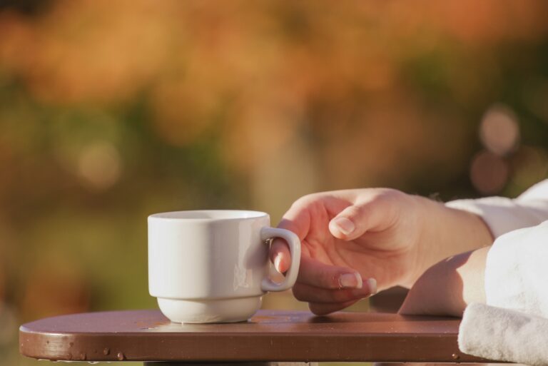 A hand takes the handle of a coffee cup, calm orange colours in the background