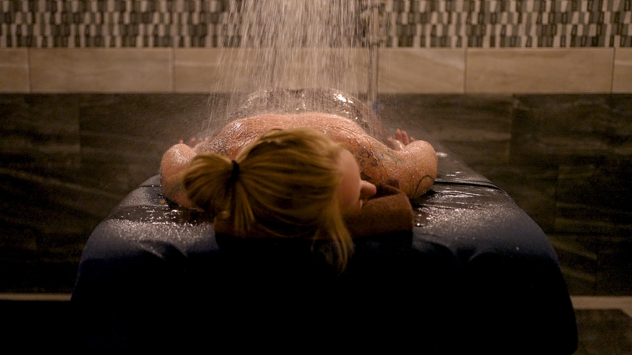 A person lays facedown on a massage table under a shower stream