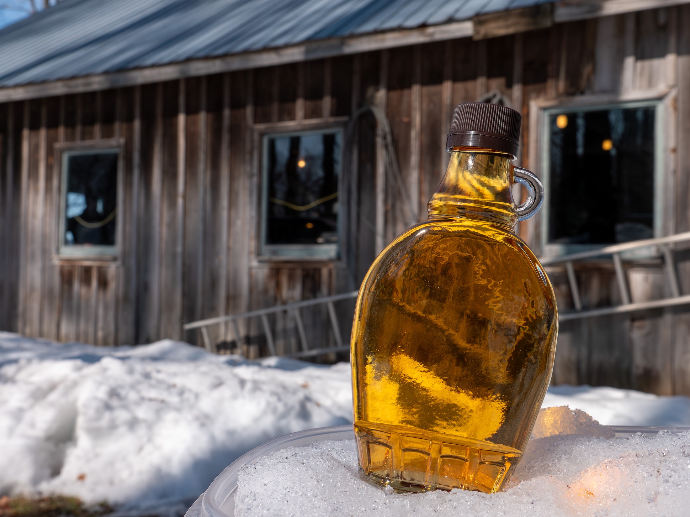 Bottle of maple syrup in snow near a wooden shed