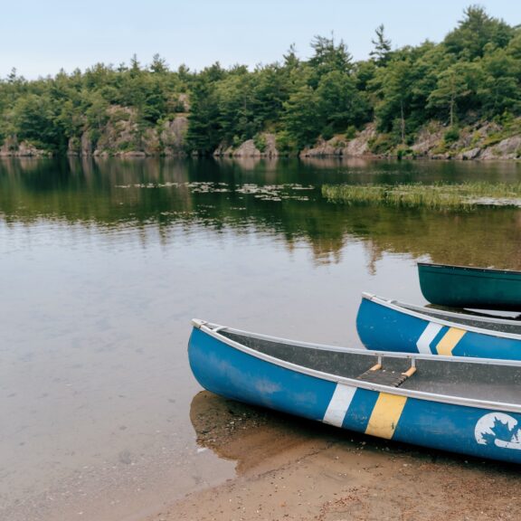 Three canoes lined up on the sandy beach of calm lake