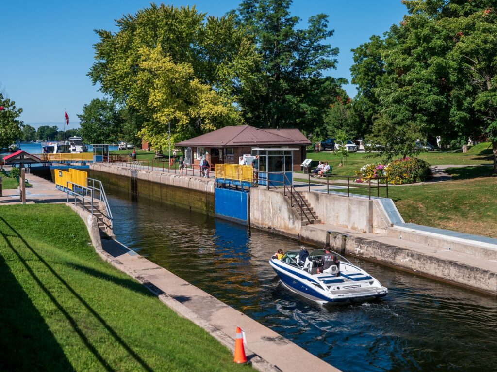 A small powerboat heads towards a lock in a concrete channel on a clear day