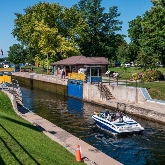 A small powerboat heads towards a lock in a concrete channel on a clear day