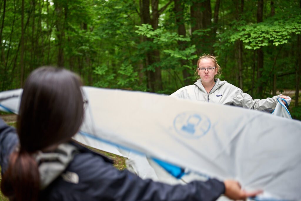 Two people spread the fly over a tent