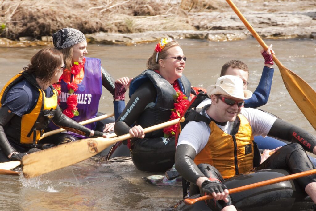 Smiling boaters with paddles in a river pass by the shore