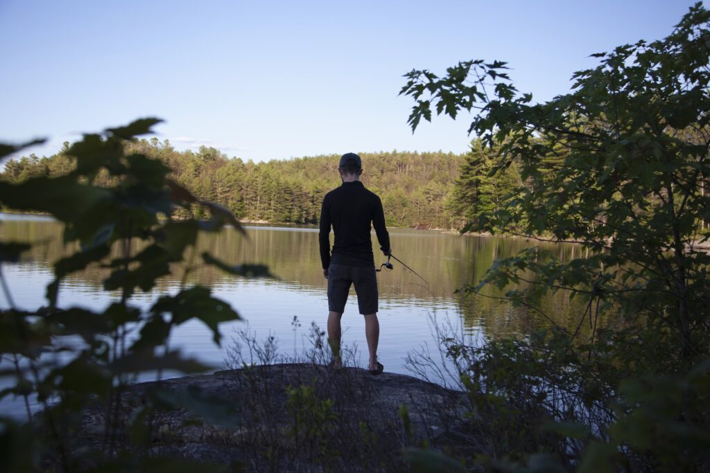 A man with his back to the camera fishes on a calm lake