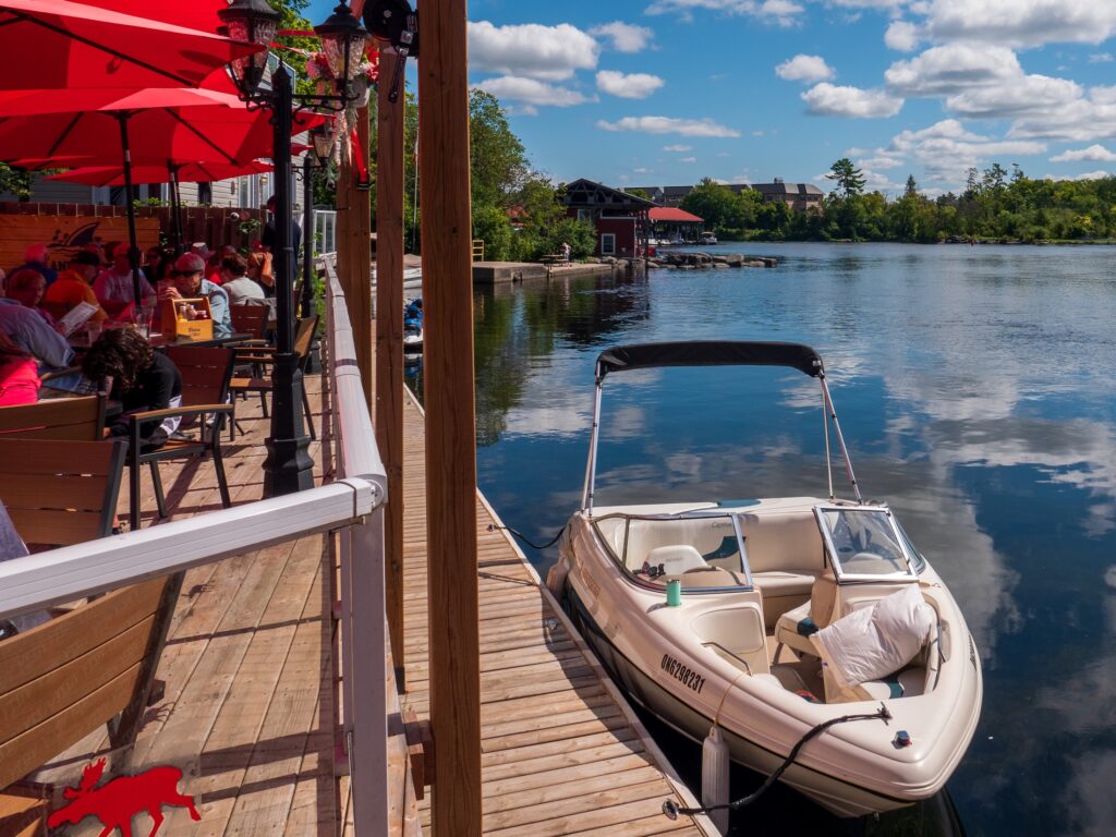 A powerboat, parked beside a restaurant patio with red umbrellas