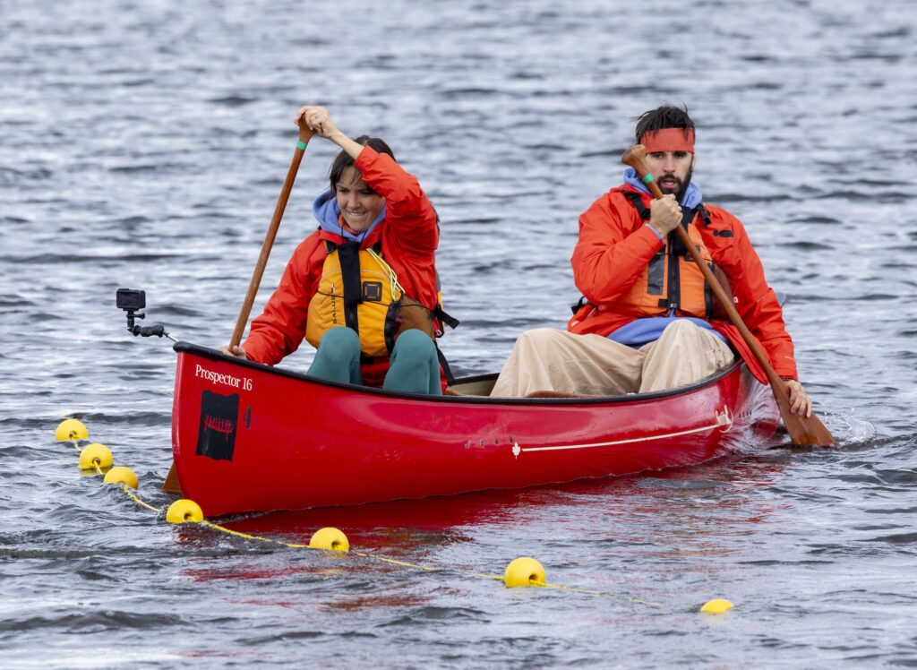 Two paddlers in a red canoe approach a line of yellow buoys