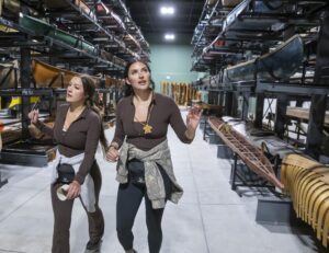 Two women walk through a museum collection hall full of canoes